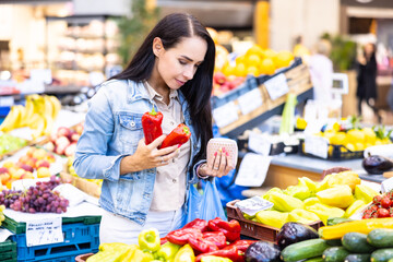 Woman shopping for vegetables holds red peppers and her purse in hands in the farmers market