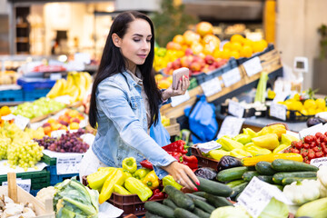 Woman shopping in the afrmers' market reaches out for a cucumber in the vegetables department