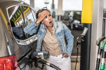 Woman refuelling the tank of her car with diesel looks shocked with mouth open seeing the high...