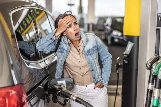 Woman refuelling the tank of her car with diesel looks shocked with mouth open seeing the high price of fuel - Powered by Adobe