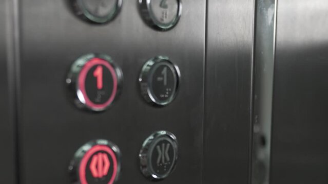 A person in elevator presses button with number one to go to first floor. The open door button is also illuminated on button panel. Woman with car keys in hand