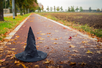 Black witch hat abandoned on a red road with autumn fallen leaves on a rainy day. Halloween...