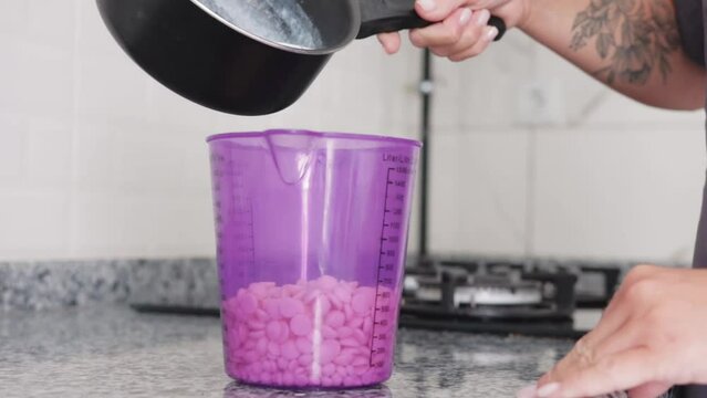 A woman pours hot milk in the container with dry mastic on the foreground