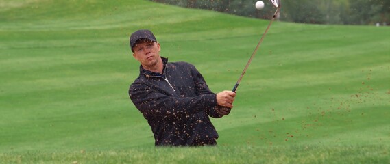 MED Caucasian male playing a bunker shot during a golf game