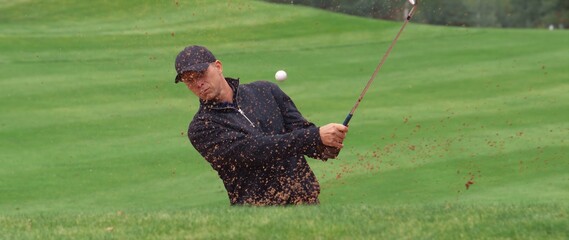 MED Caucasian male playing a bunker shot during a golf game