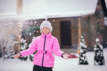 Beautiful girl playing with snow in winter forest. Smiling girl  having fun with snow falling in hands. Fashion young woman in the winter park. Christmas.