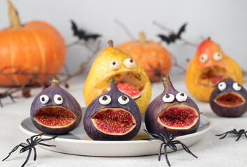 Spooky pear and fig monsters for Halloween party on gray background decorated with spiders and bats, Halloween Fruit Serving Idea