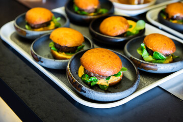 A pile of beef burgers with cheese and lettuce ready to be served by the waiters at an event, a birthday in a restaurant.