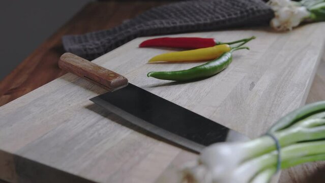 Slow dollie shot of wooden cutting board with green onions, knife and fresh chili peppers.

