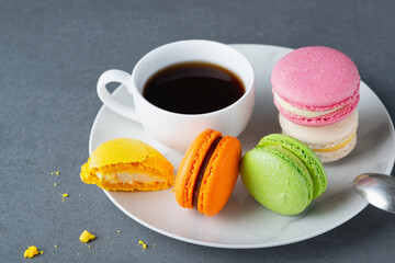 French colored macaroons with white cup of coffee on grey background