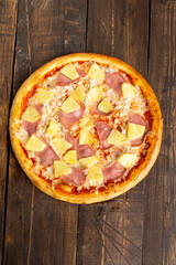 Pizza with ham and pineapple. On a wooden table.