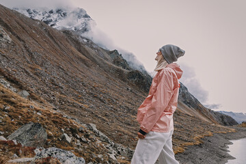 Young woman tourist enjoys mountain view next to mountain lake in tourist clothes