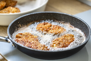 Sizzling hot oil with schnitzel frying in it in a dark pan