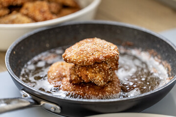 Schnitzels in breadcrumbs piled on a black pan full of frying oil