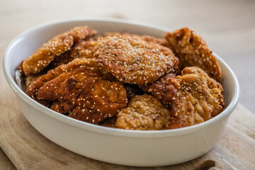 White bowl full of breaded meat schnitzels with sesame seeds