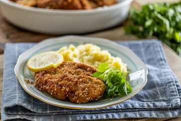 Schnitzel with sesame seeds served with potato mash and greens on a plate