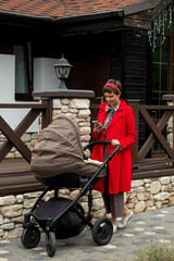 Young mother in a red coat walks with a stroller and reads news on her phone.