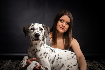 A young pretty woman is playing with her Dalmatian pet, isolated on a black background.