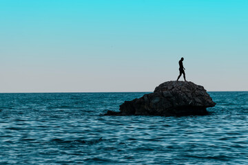A man on a lonely stone island in the middle of the sea.