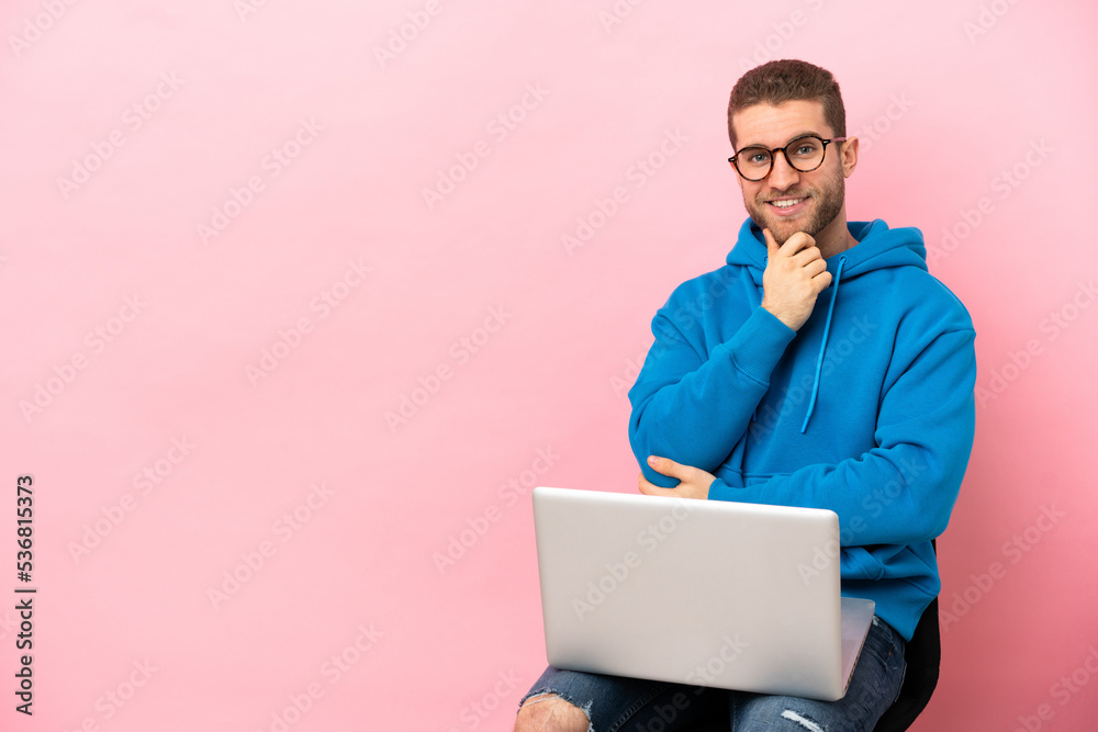 Poster Young man sitting on a chair with laptop with glasses and smiling