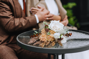 A wedding bouquet of wild flowers, reeds lies on the table, against the background of the newlyweds embracing.