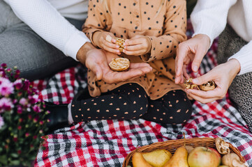 A happy, loving family sits on a plaid with a walnut in their hands close-up. Photo of father, mother and child, daughter in nature in the forest.