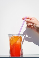 refreshing summer cocktail. A cold orange drink in a takeaway glass against a wall background. Sale of summer drinks lifestyle