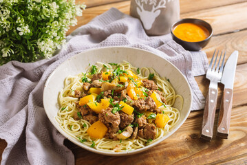 Egg noodles with chunks of yellow bell peppers and homemade minced meat, sprinkled with chopped parsley. Homemade hearty lunch in natural colors. Fork and knife with wooden handles.