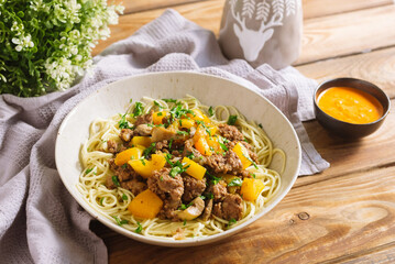 Egg noodles with chunks of yellow bell peppers and homemade minced meat, sprinkled with chopped parsley. Homemade hearty lunch in natural colors. Fork and knife with wooden handles.