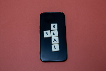Be real text with plastic letters on smart phone. Popular and trendy mobile app called Be Real is spreading around the globe. Be realistic yourself is a good way of living your life.