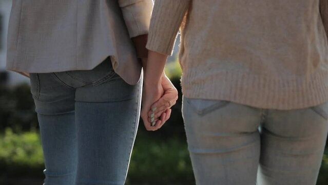 A lesbian couple gently and boldly takes hands in the middle of a street in the city. LGBT concept, pride, freedom, diversity, politeness