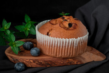 blueberry muffin and fresh scattered blueberries with on a dark surface.