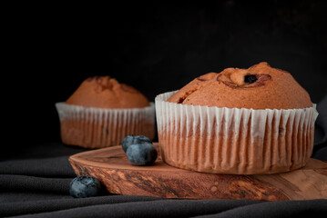 blueberry muffin and fresh scattered blueberries with on a dark surface.