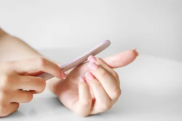  A girl with beautiful long nails makes a manicure with a nail file on a white background, close up of hands © RaspberryStudio