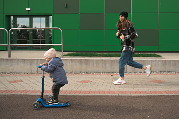 Mother help her son ride with kick scooter. Happy family mother teaches child son to ride a scooter in the Park. Support childhood parenthood idea. happy family concept - 536826102