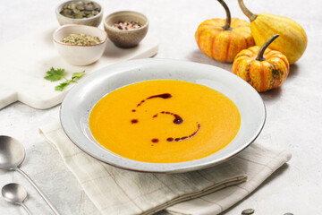 One deep grey soup bowl with an orange pumpkin cream soup with pumpkin seed oil, on a gray concrete background