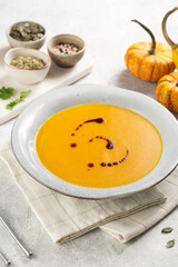 One deep grey soup bowl with an orange pumpkin cream soup with pumpkin seed oil, on a gray concrete background