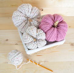 beige and soft pink colored crochet woolen pumpkins on wooden ground in a basket with crochet hook and woolen ball