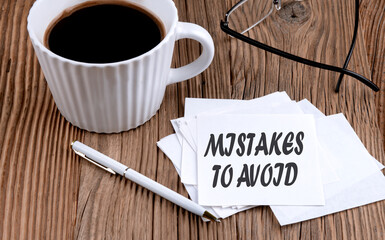MISTAKES TO AVOID text on sticky with coffee and pen on wooden background