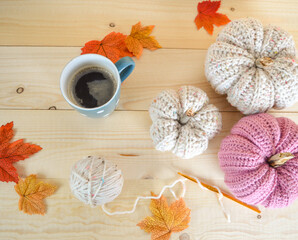 natural and soft pink colored crochet woolen pumkins on wooden ground with woolen ball, crochet hook and a mug of coffee
