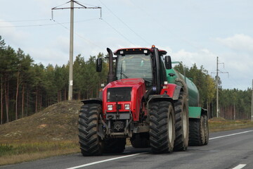 Fototapeta premium Big red wheeled tractor with barrel drive on country highway road