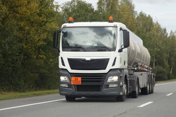 Fototapeta na wymiar White semi truck barrel truck with 30-1202 dangerous goods class sign drive on suburban highway road at autumn day, front view, diesel fuel ADR cargo transportation logistics