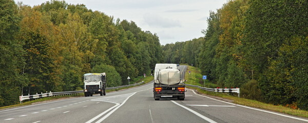 Barrel truck transportate a liquid food goods on suburban highway road in forest at autumn day , back  view