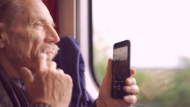 Elderly man traveling by train and taking pictures of the landscape through the window using a smartphone