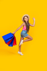 happy teen girl hurry up with shopping bags on yellow background. full length