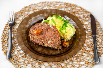 Baked minced beef, garlic and mashed potato on plate, cutlery and bamboo pad.