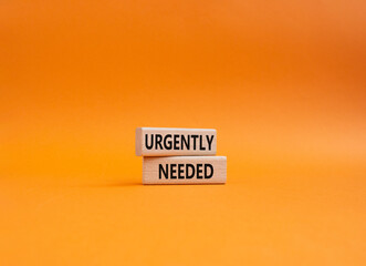 Urgently needed symbol. Concept word Urgently needed on wooden blocks. Beautiful orange background....