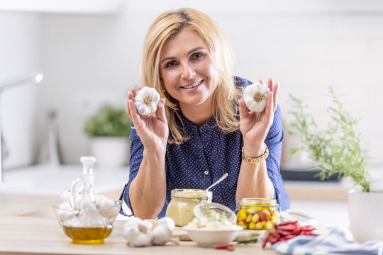 Woman holds garlic heads in her hands while various types of garlic preserves surround her
