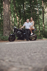 Fototapeta na wymiar Young beautiful couple hugging, sitting on a motorcycle, travel together on a forest road
