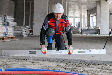 A foreman at a construction site in work clothes controls the work process, takes the necessary measurements